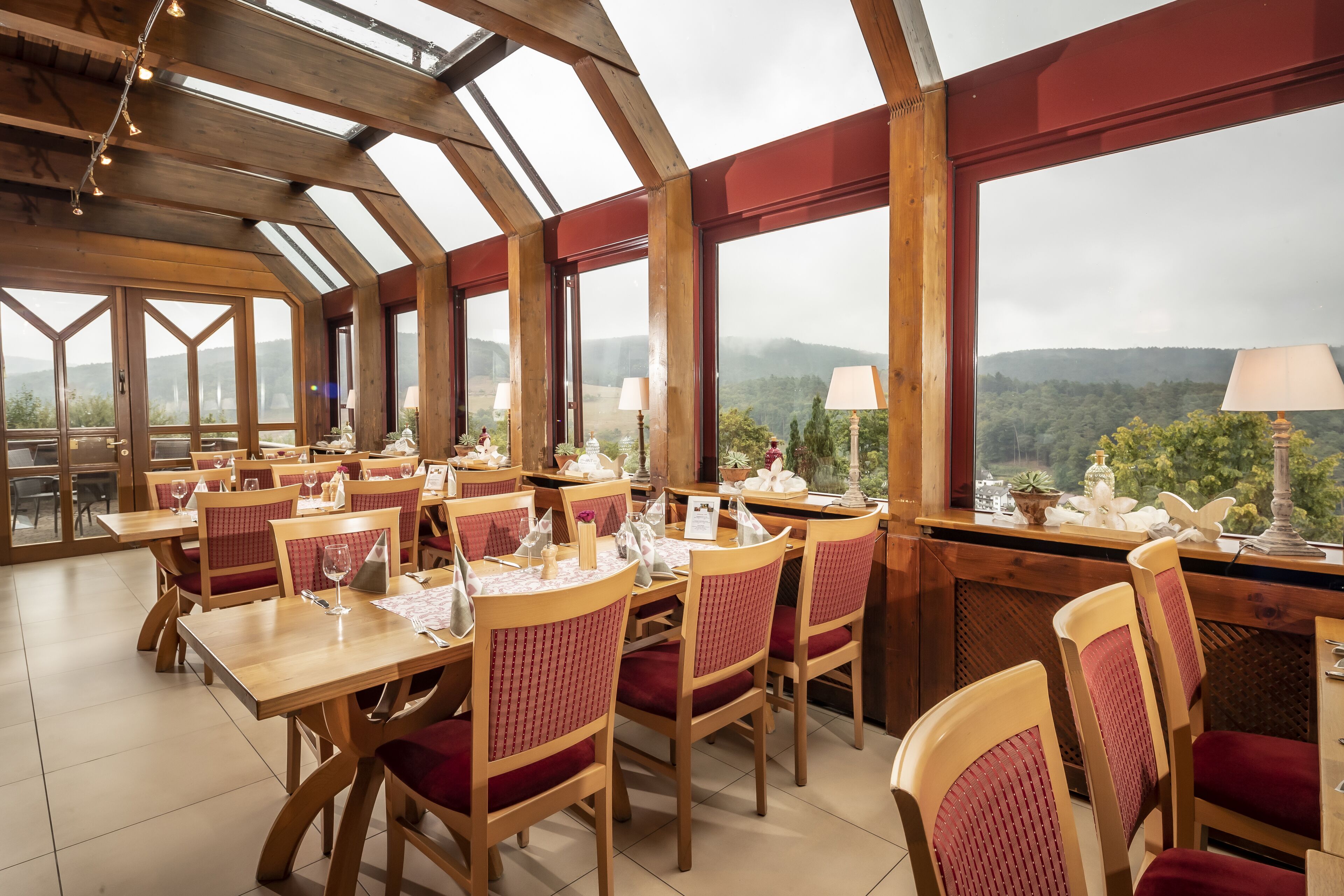 A restaurant with wooden tables and chairs, large windows, and a view of the mountains.