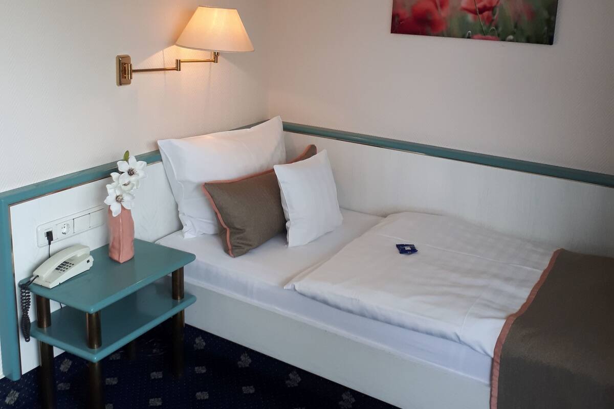 Una habitación de hotel con una cama, una mesita de noche con lámpara, un teléfono y un cuadro en la pared.