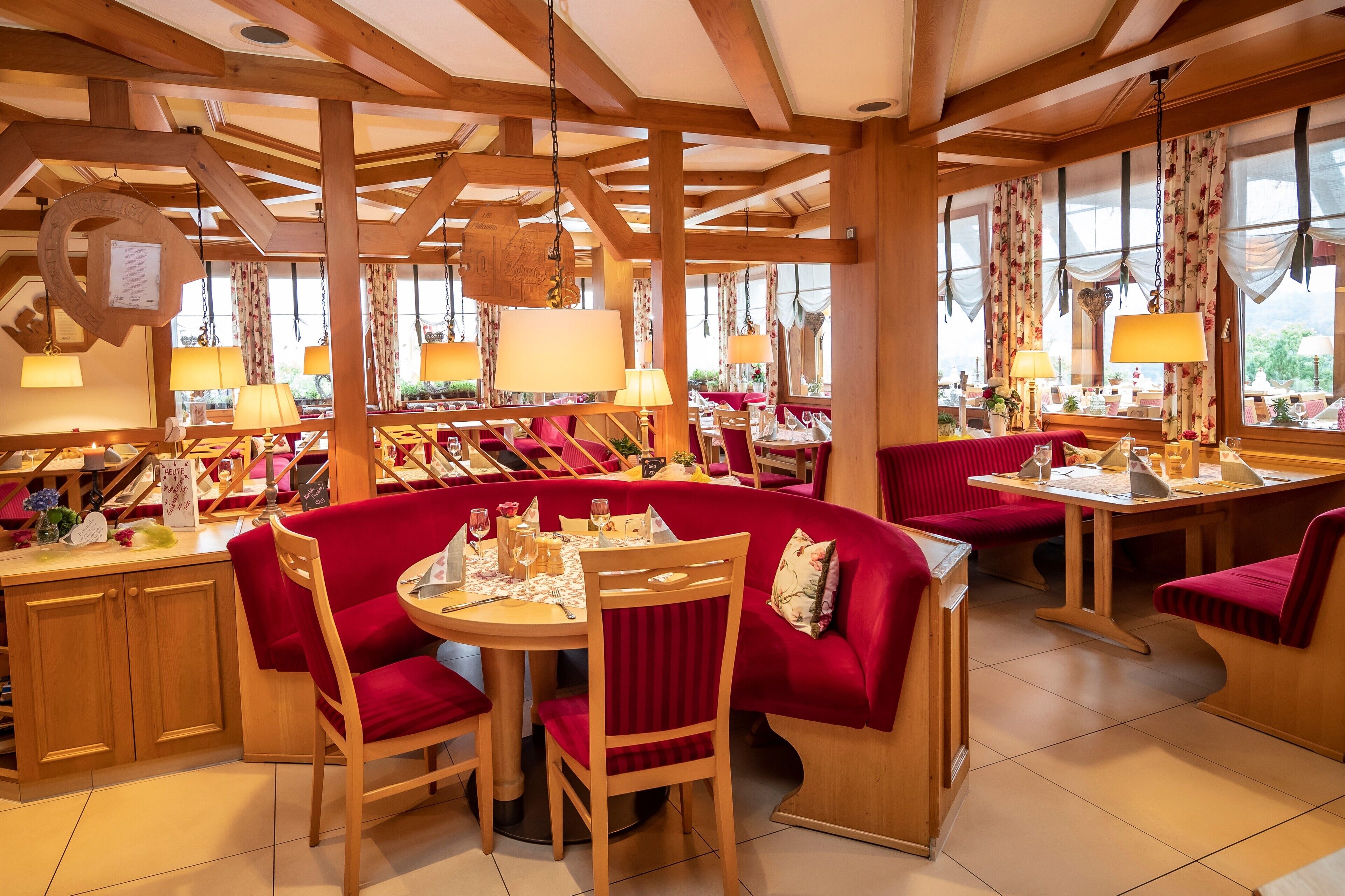A restaurant with wooden beams, red upholstered booths, and hanging lamps.