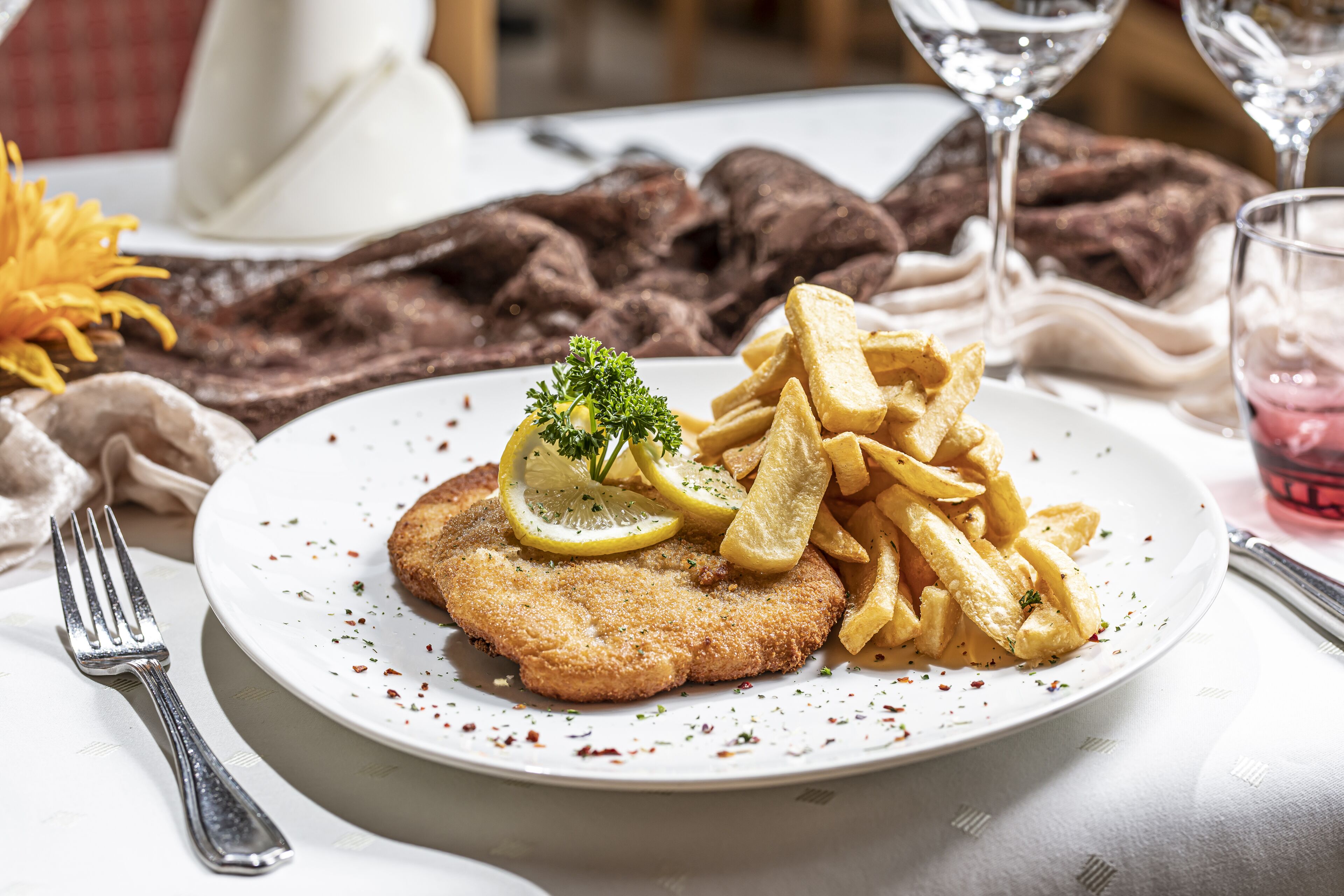 A plate with a breaded cutlet, lemon slices, and fries.