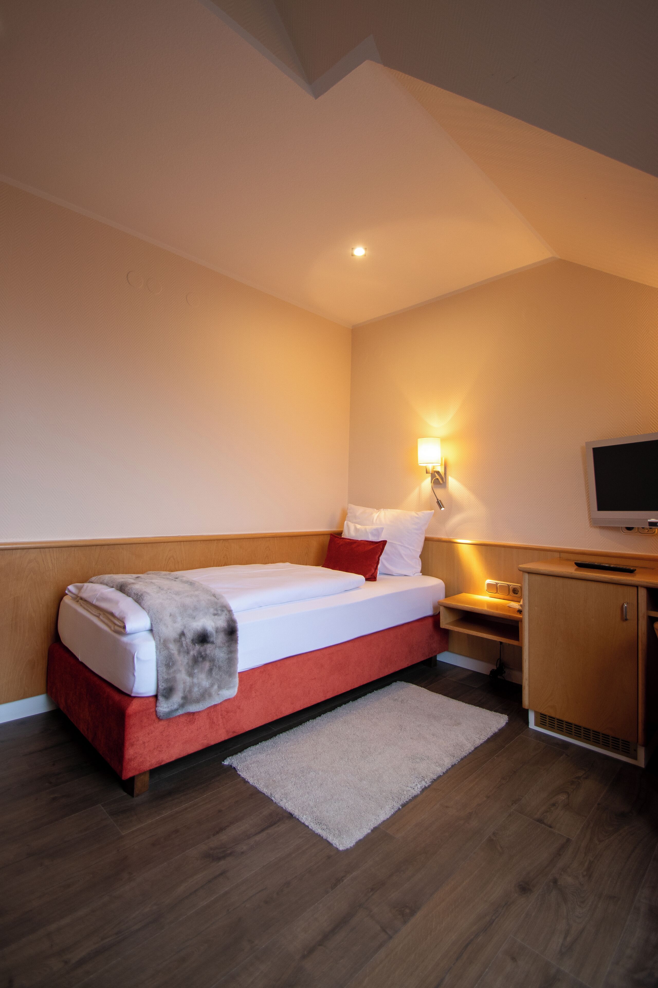 Une chambre d’hôtel avec un lit, une table de chevet, un téléviseur et une armoire en bois.
