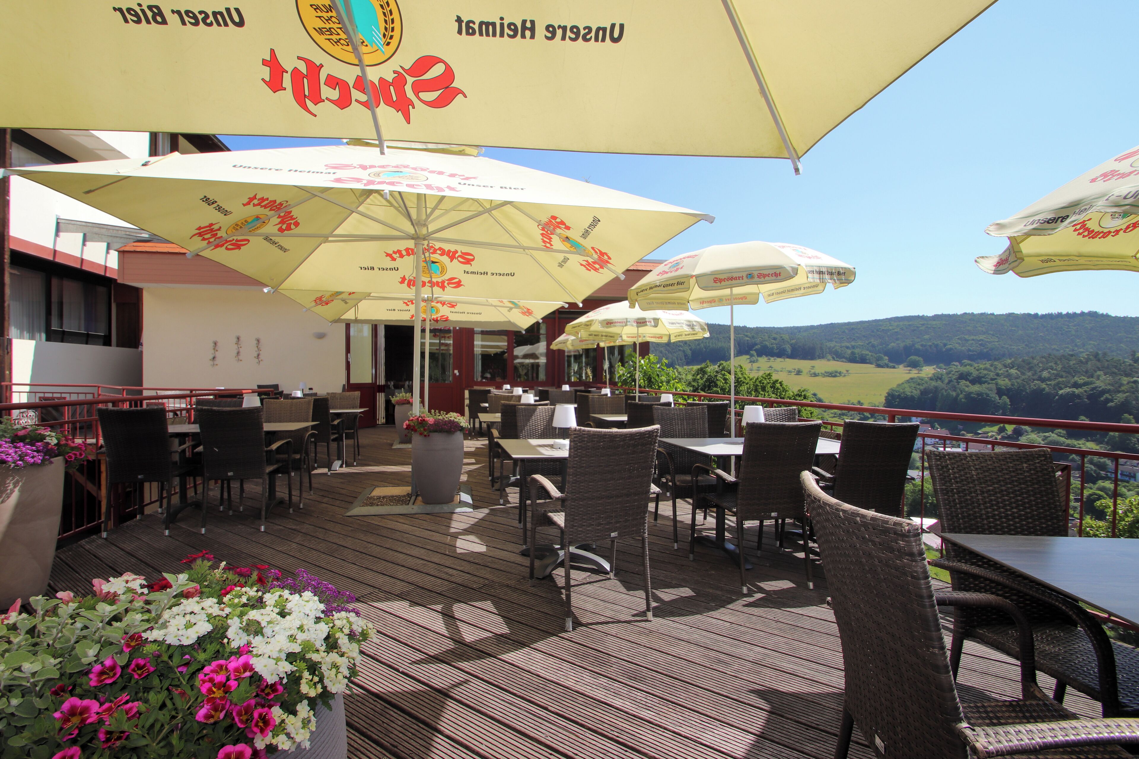An outdoor patio with wicker furniture and umbrellas, overlooking a scenic landscape.