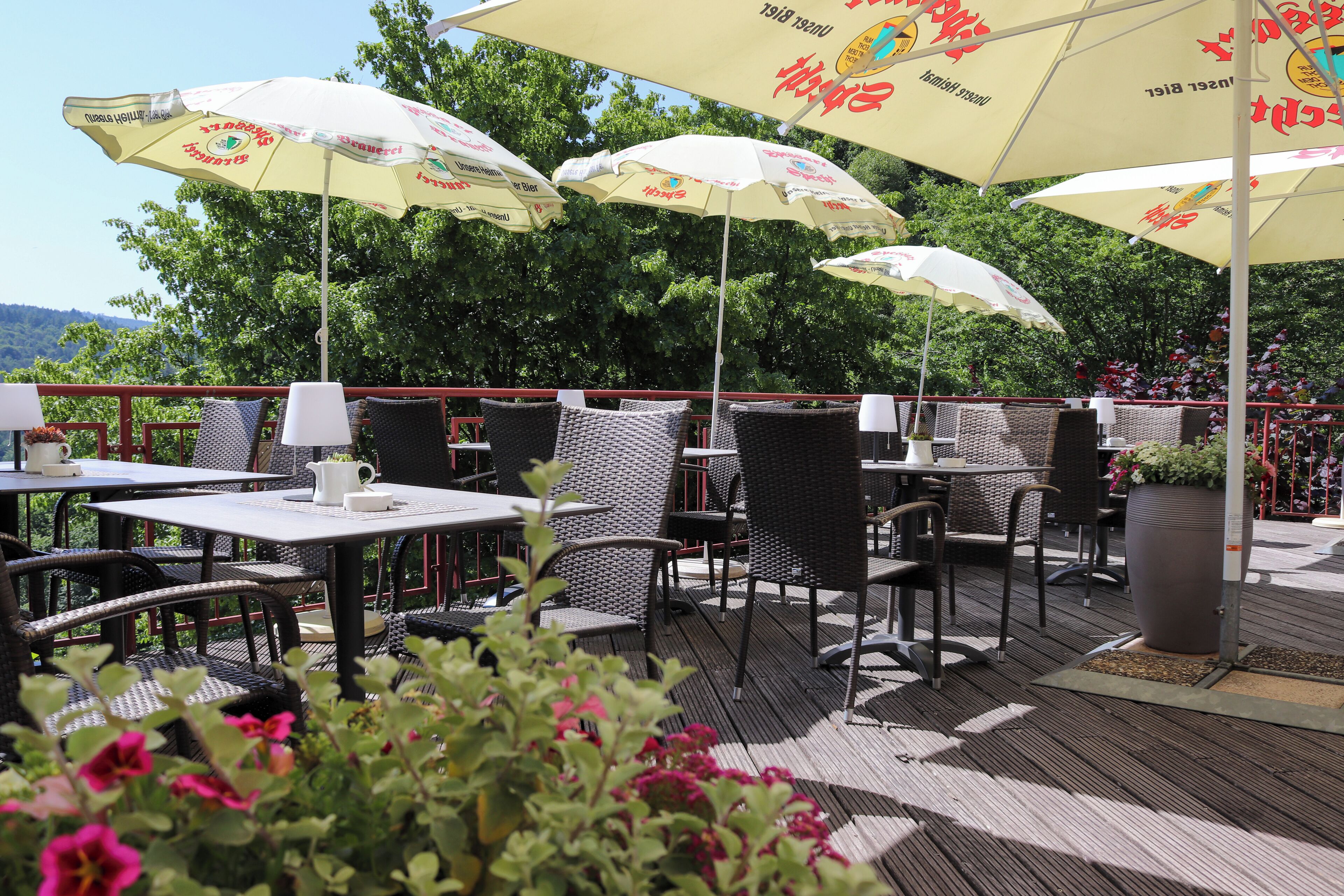 An outdoor seating area with tables and chairs, umbrellas, and a view of trees and hills.