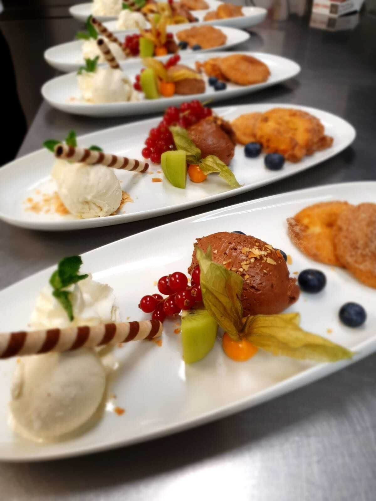 Eine Reihe weißer Teller mit Desserts, darunter Eis und Früchten.