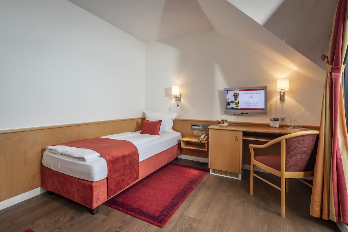 Habitación de hotel con cama, escritorio, silla, televisor y un tapete rojo.
