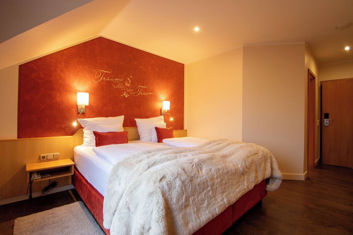 Habitación de hotel con una cama grande, dos lámparas de noche, una mesita de noche y una pared de acento roja con un letrero decorativo.