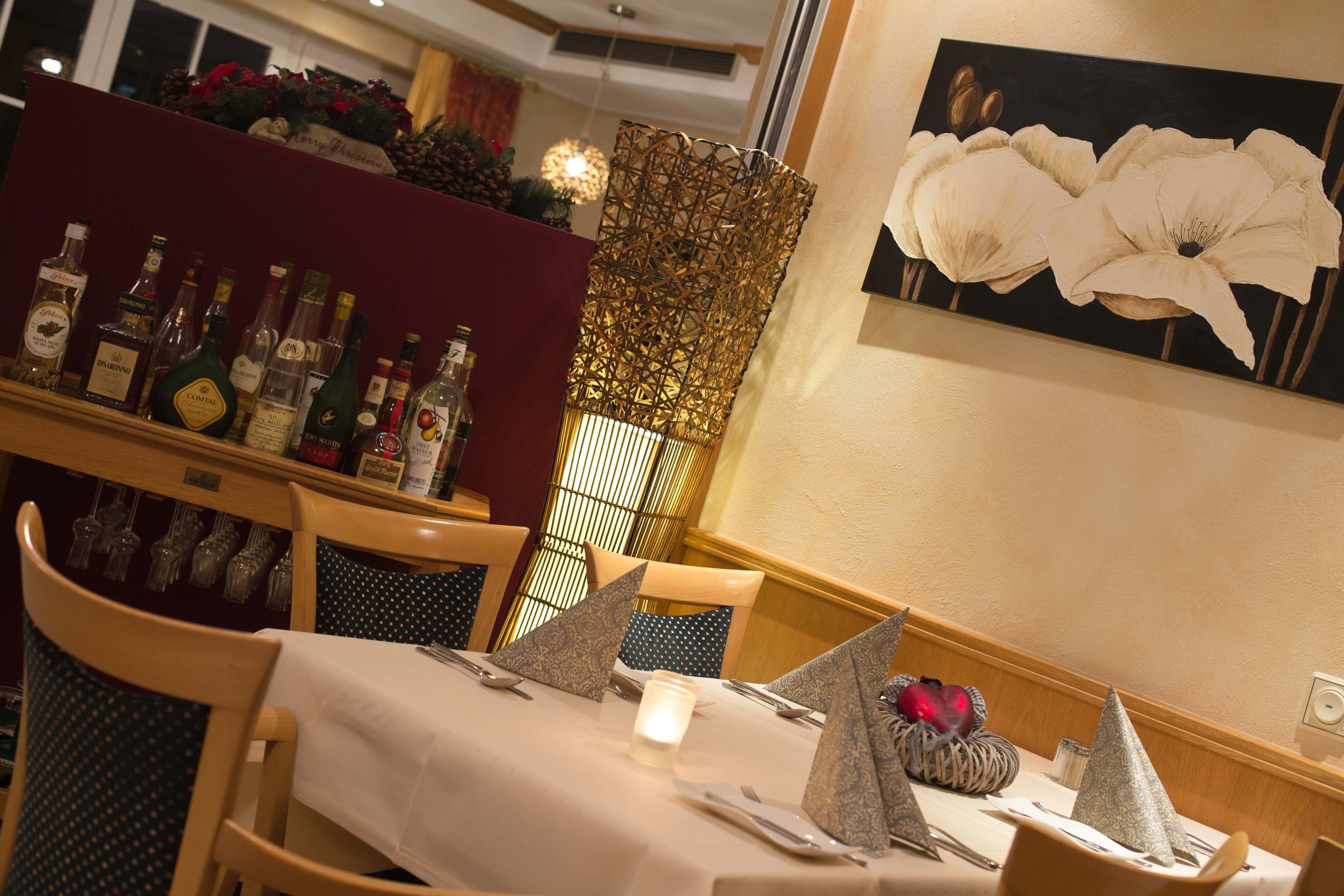A dining area with a table set for two, a decorative wall with a floral painting, and a bar area with various bottles.