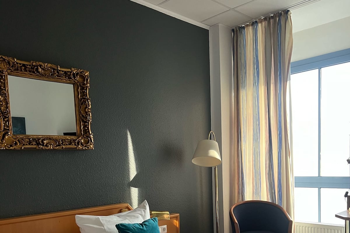 Ett hotellrum med en stor säng, ett nattduksbord, en lampa, en stol och ett fönster med gardiner.