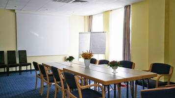 A conference room with a long table, chairs, a projector screen, and a flower vase.