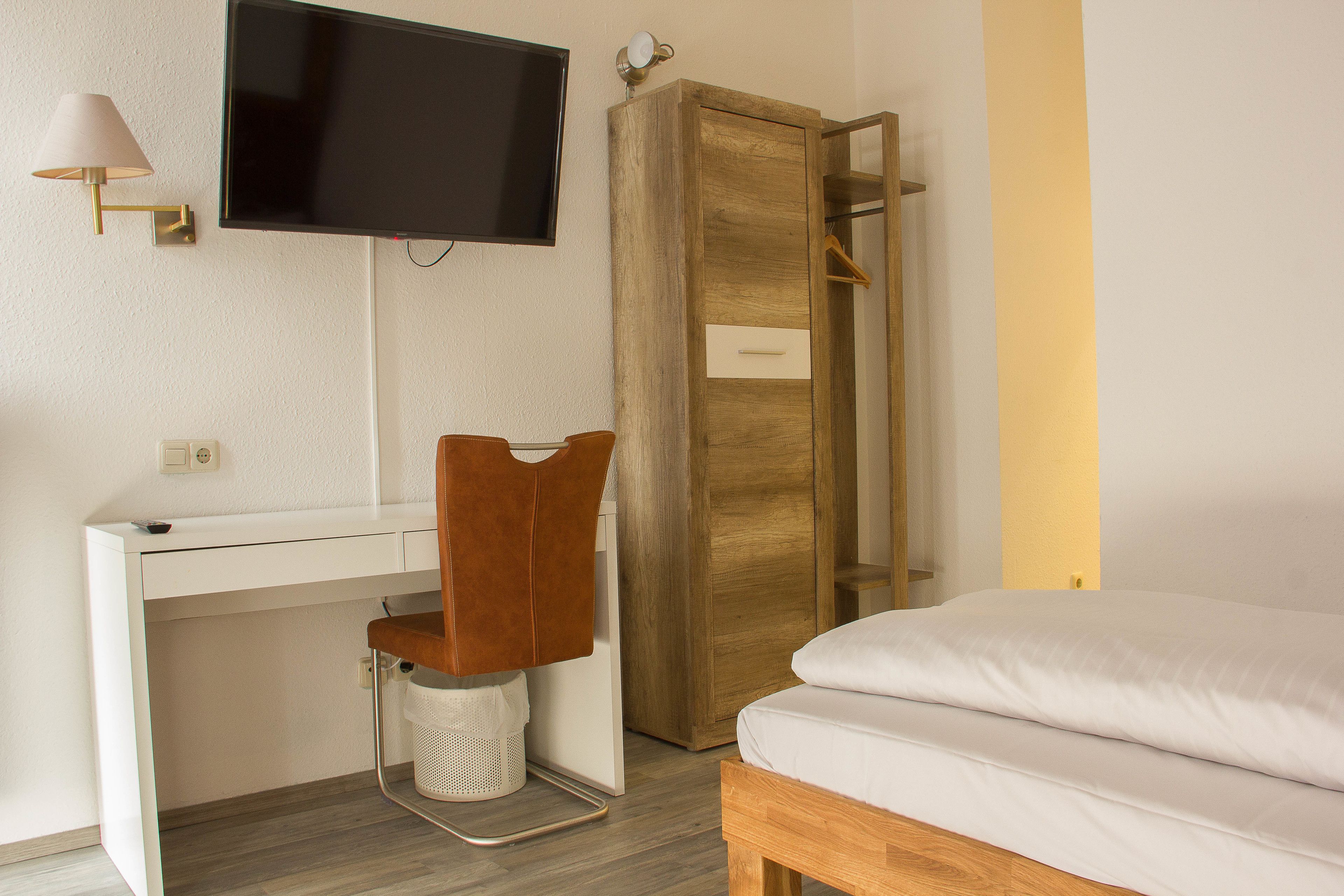 A bedroom with a bed, a desk with a chair, a television, and a wardrobe.