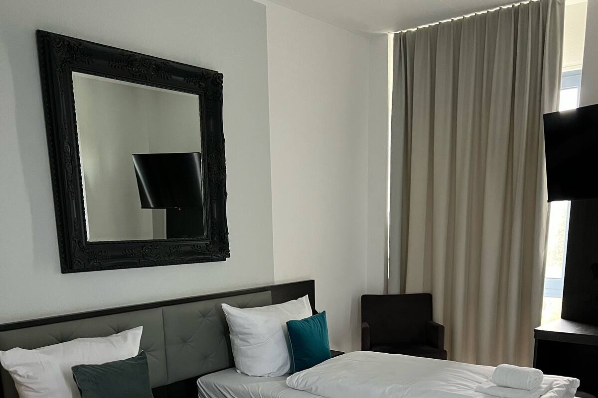 Ett hotellrum med två sängar, en stor spegel, en tv och ett fönster med gardiner.