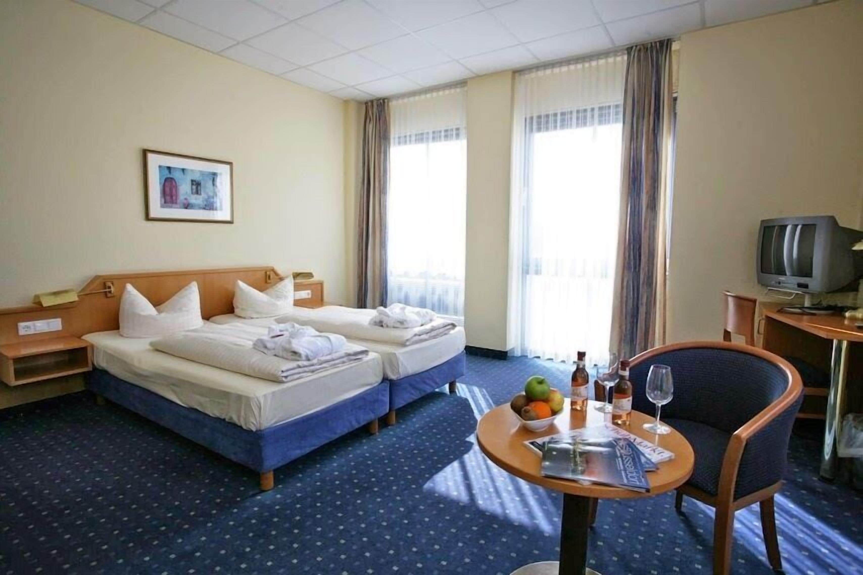Een hotelkamer met twee bedden, een tafeltje met een schaal fruit en flessen, een stoel, en een televisie op een bureau.