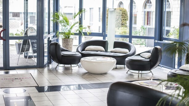 Un hall moderno con sofás de cuero negro, una mesa de centro blanca y una planta grande en maceta.