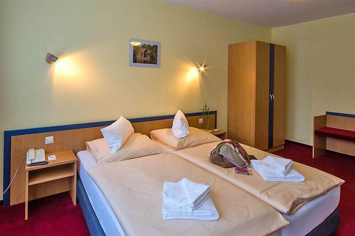 A hotel room with two beds, a wardrobe, a bedside table with a lamp, and a small picture on the wall.