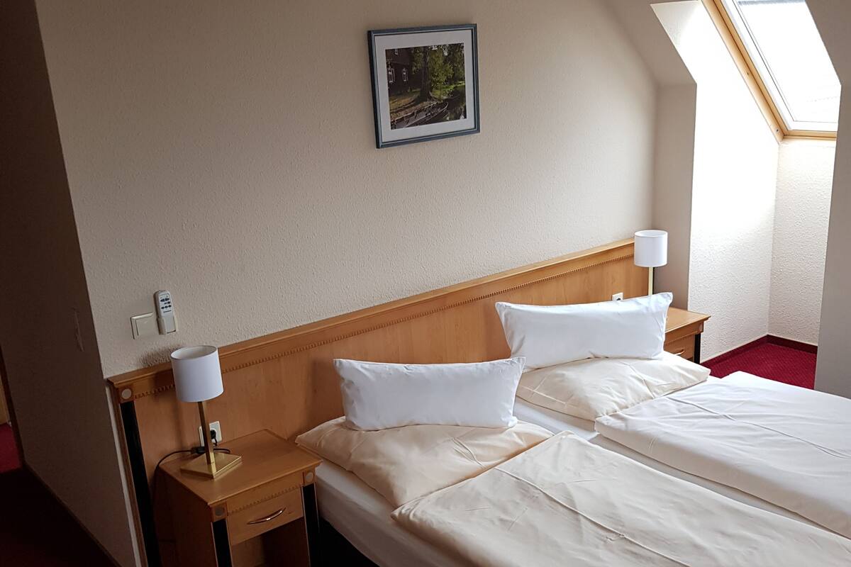 A hotel room with a bed, bedside tables, a ceiling fan, a window, and a framed picture on the wall.