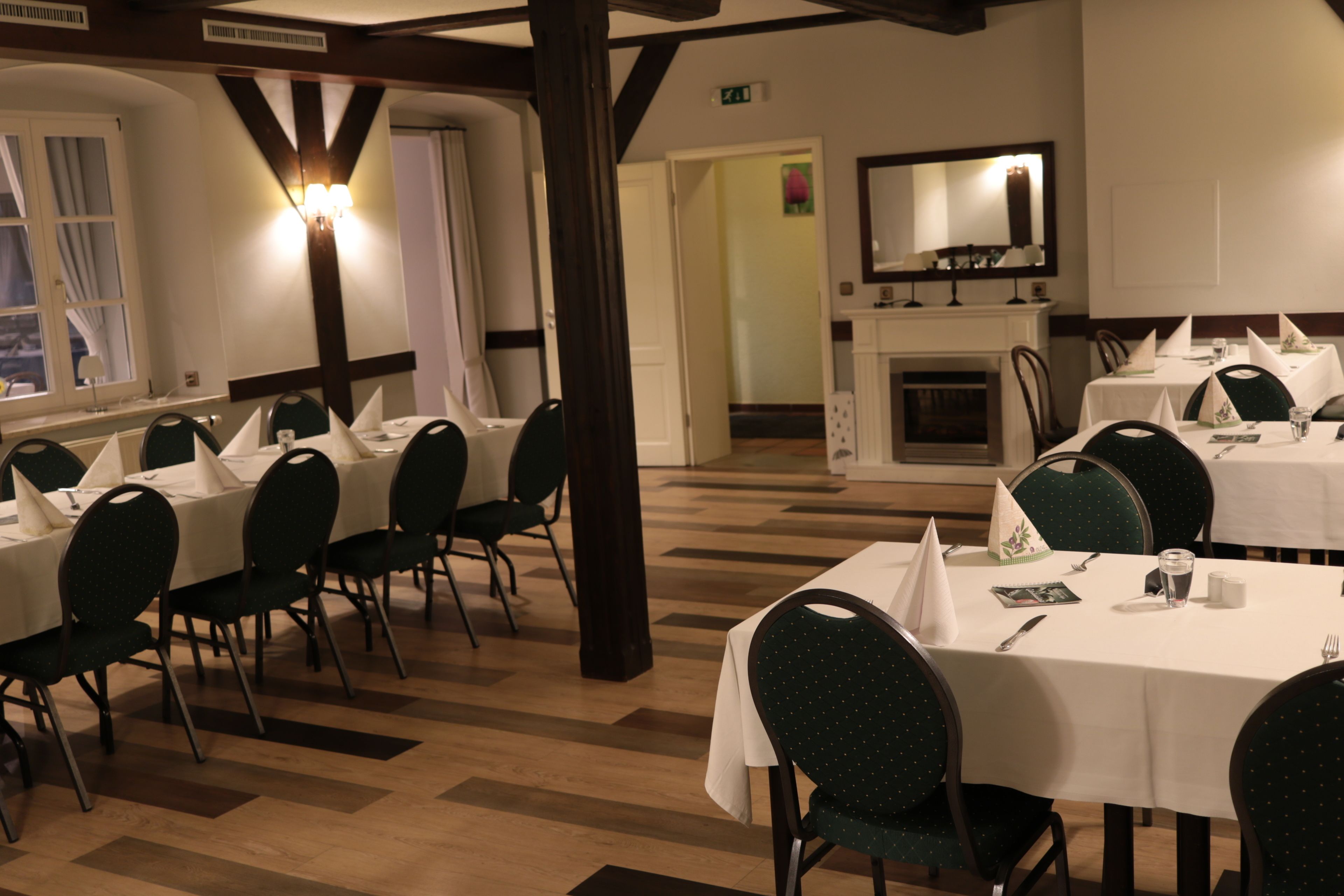 A hotel dining area with multiple tables and chairs, a fireplace, and a large mirror on the wall.