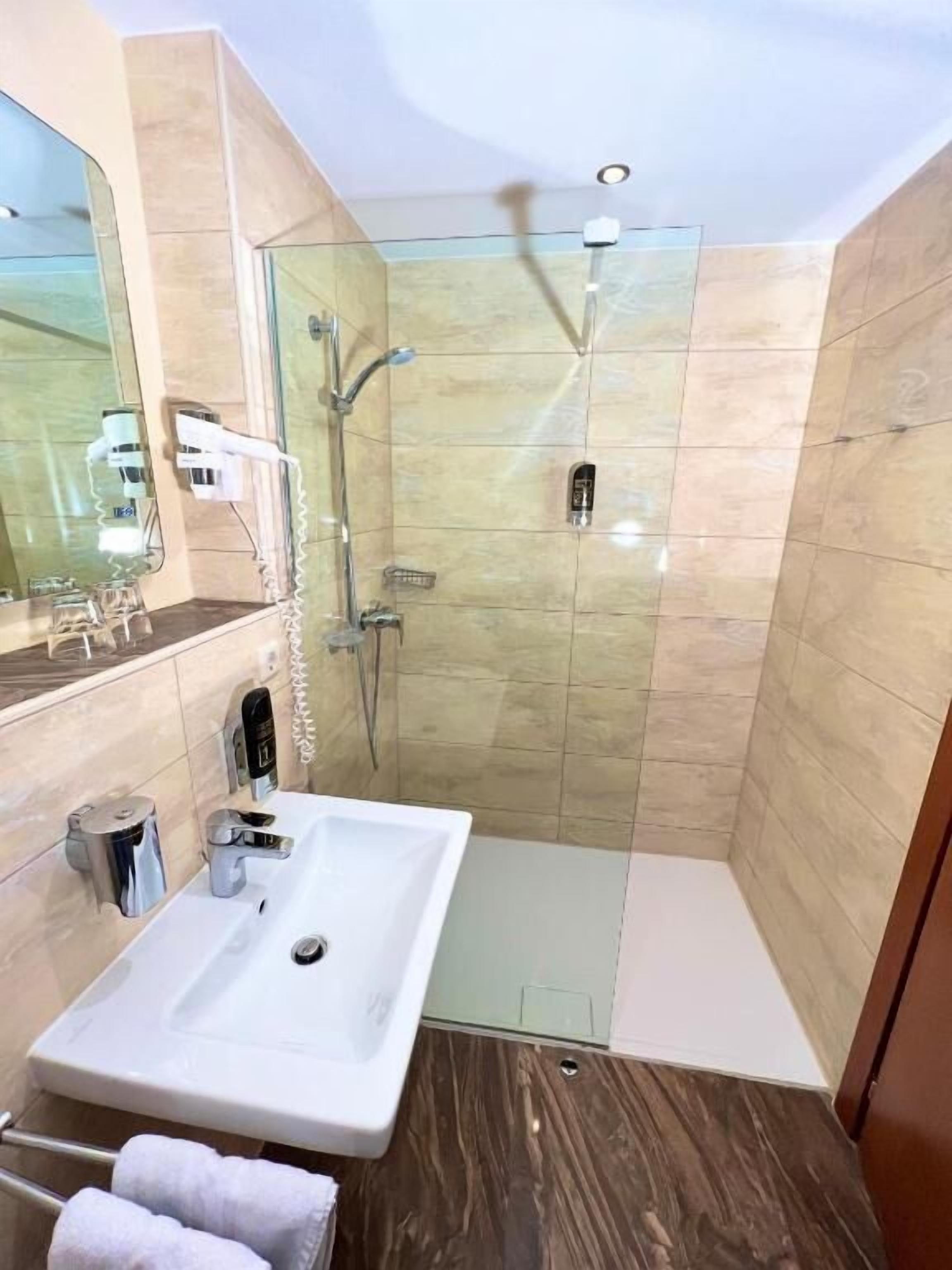 Un baño moderno con ducha de vidrio, un lavamanos blanco y un espejo.