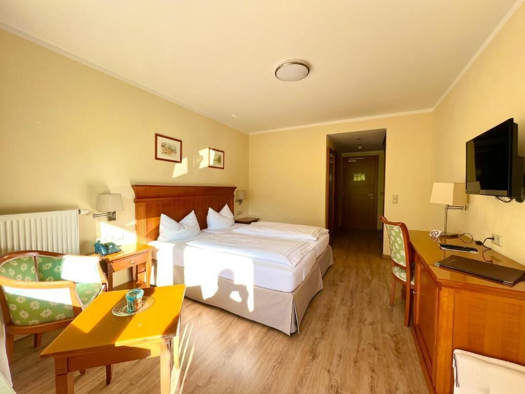 Habitación de hotel con cama doble, escritorio de madera, una silla, una mesita, televisor y radiador.