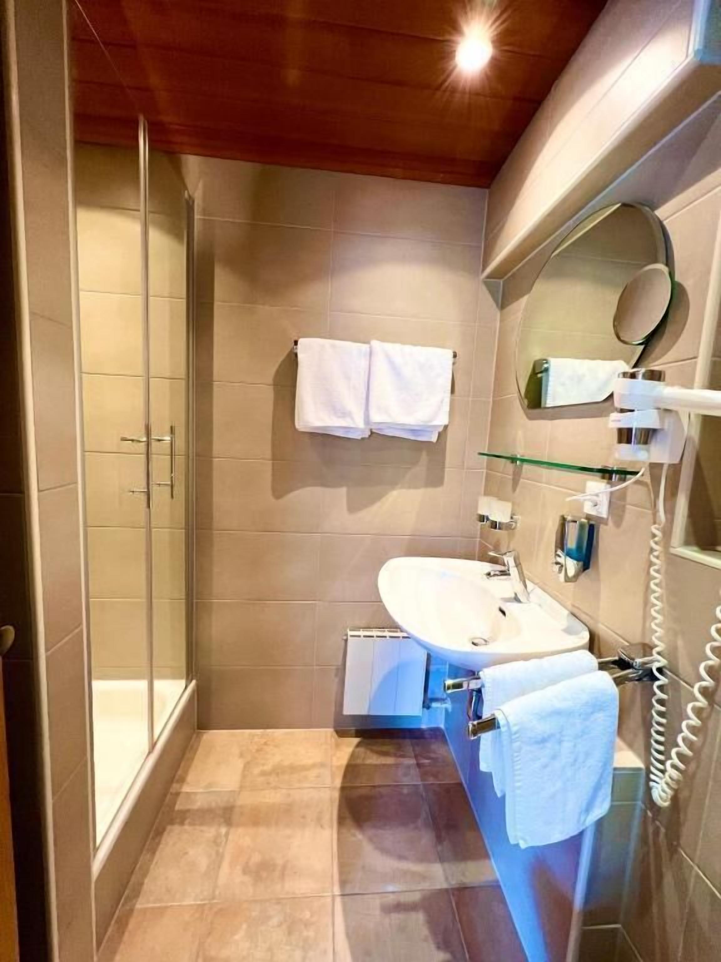 A bathroom with a glass shower enclosure, a sink with a mirror, and two towels hanging on the wall.