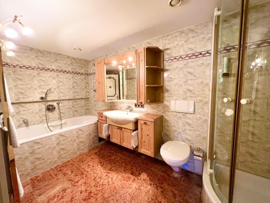 A bathroom with a bathtub, sink, and toilet, wooden cabinets, and a glass shower enclosure.