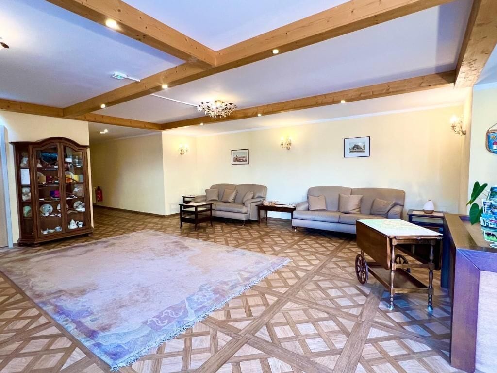Un salon spacieux avec un plafond haut, des poutres apparentes, deux canapés, une table basse, un tapis et un meuble avec des portes en verre.