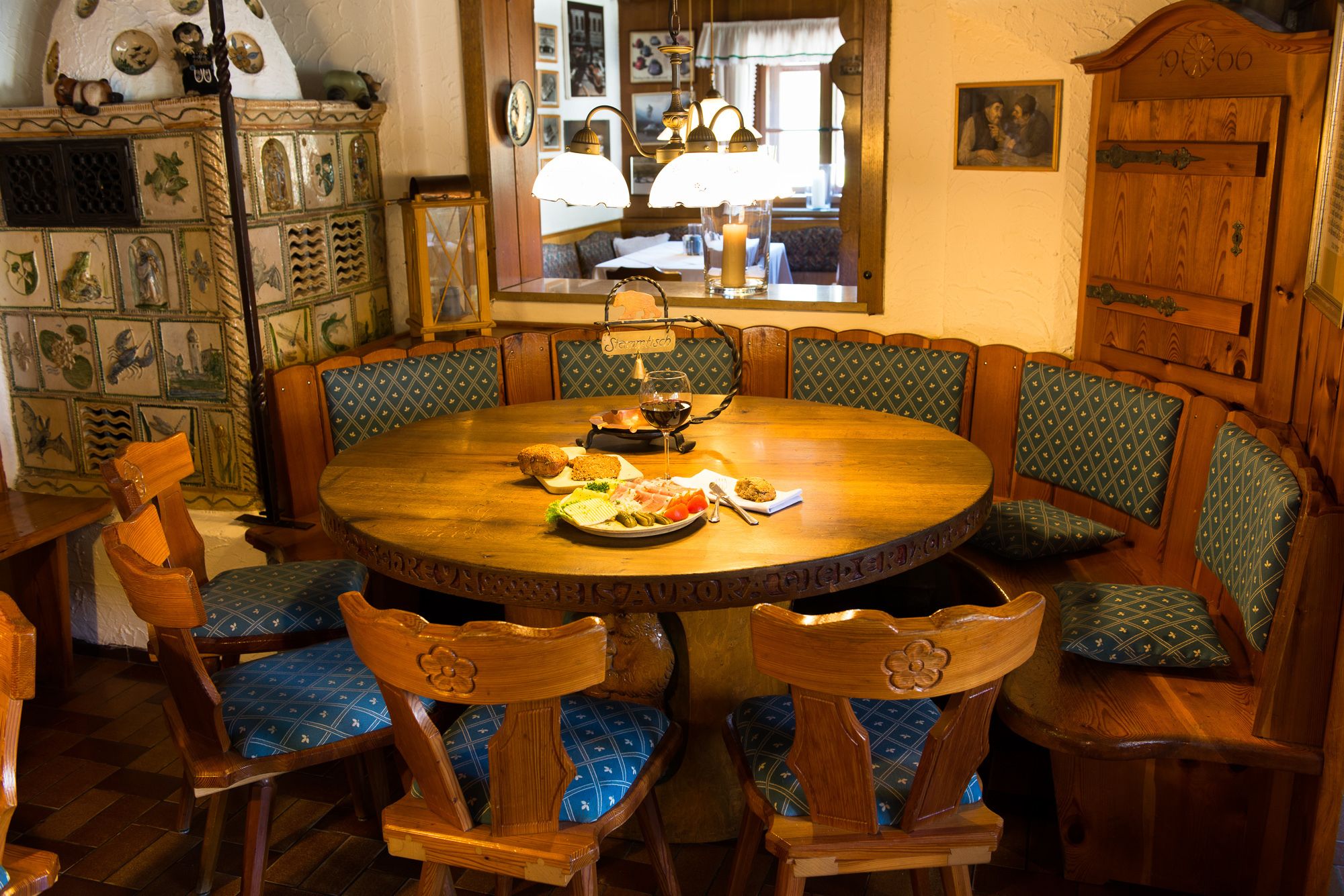 A round wooden dining table with a glass top, surrounded by wooden chairs with blue patterned cushions.