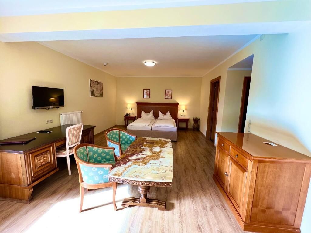 Una habitación de hotel con una cama, un escritorio con una silla, una mesa de comedor con sillas y un televisor fijado a la pared.