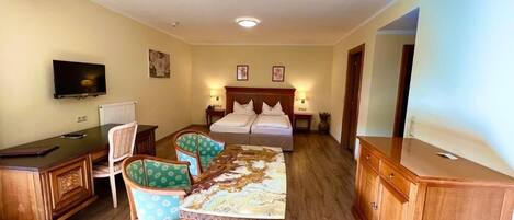Una habitación de hotel con una cama, un escritorio con una silla, una mesa de comedor con sillas y un televisor fijado a la pared.