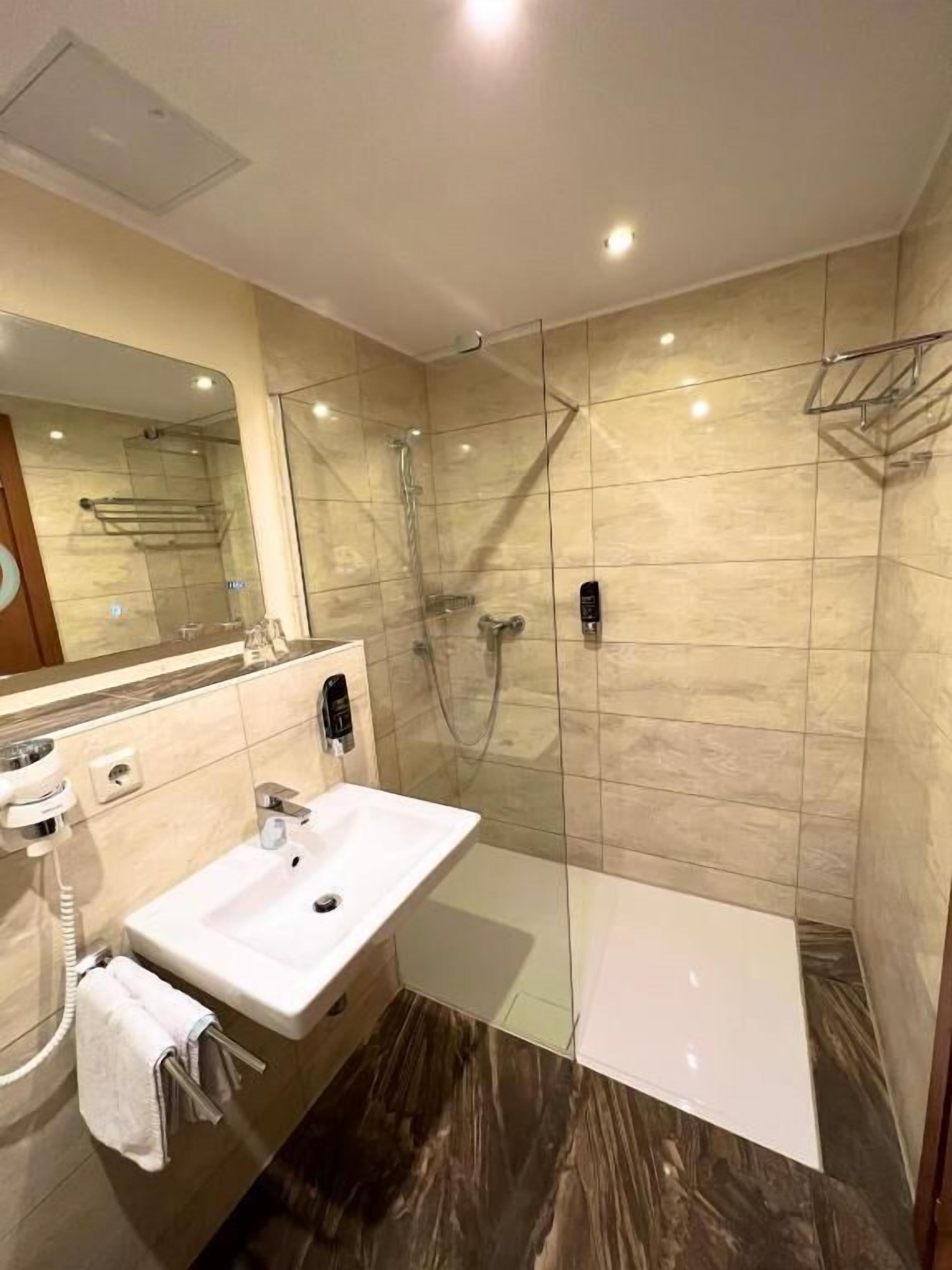 A modern bathroom with a glass-enclosed shower, a white sink, and a mirror.