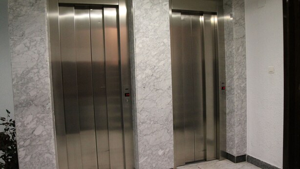 Two elevator doors in a lobby with marble walls and a tiled floor. - Pensión Terminal (Málaga)