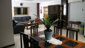 A living room with a sofa, a dining table with chairs, a potted plant, and a fireplace. - Pensión Terminal (Málaga)