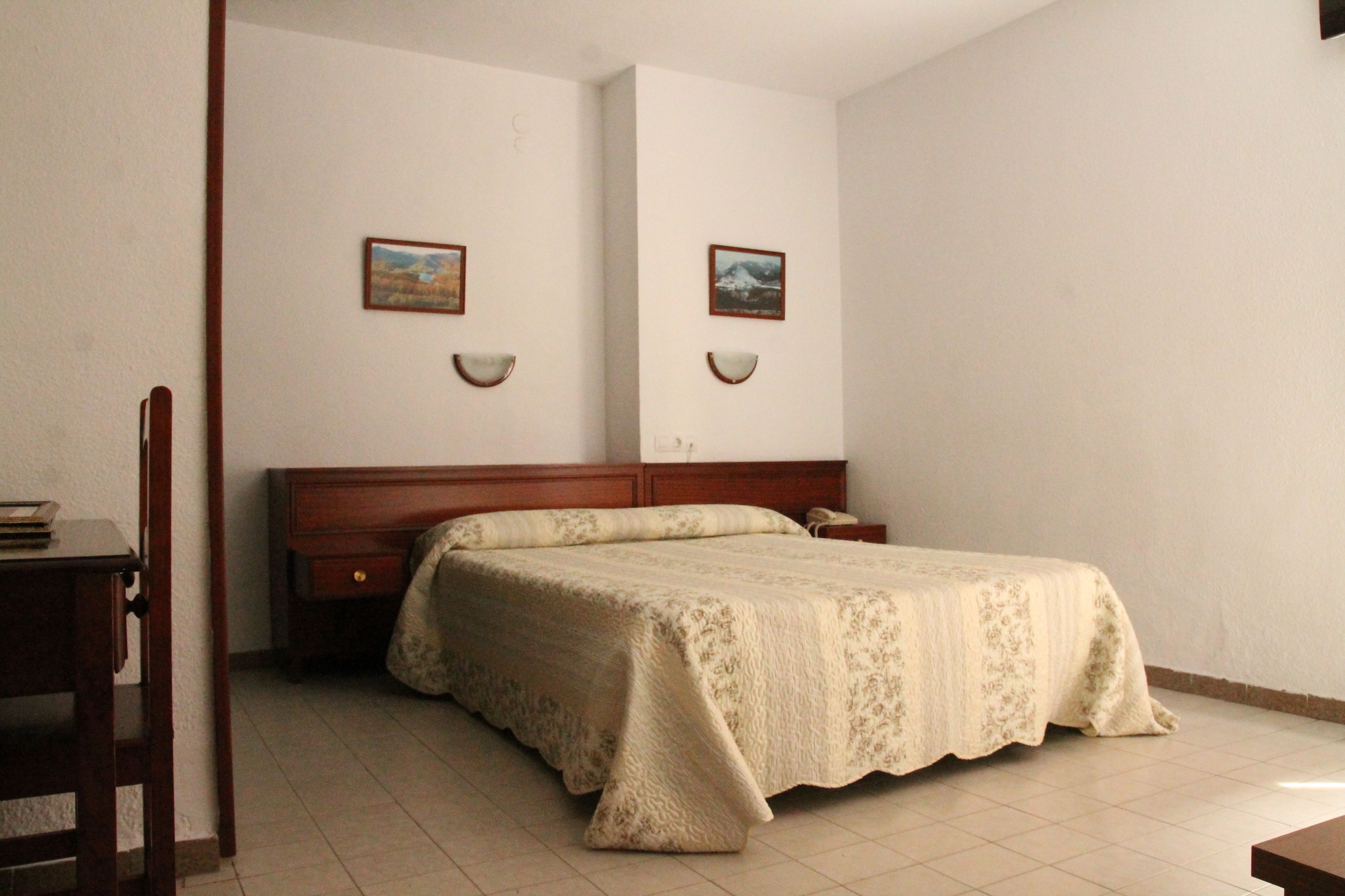 A bedroom with a bed, a wooden nightstand, a chair, and two wall-mounted lamps.
