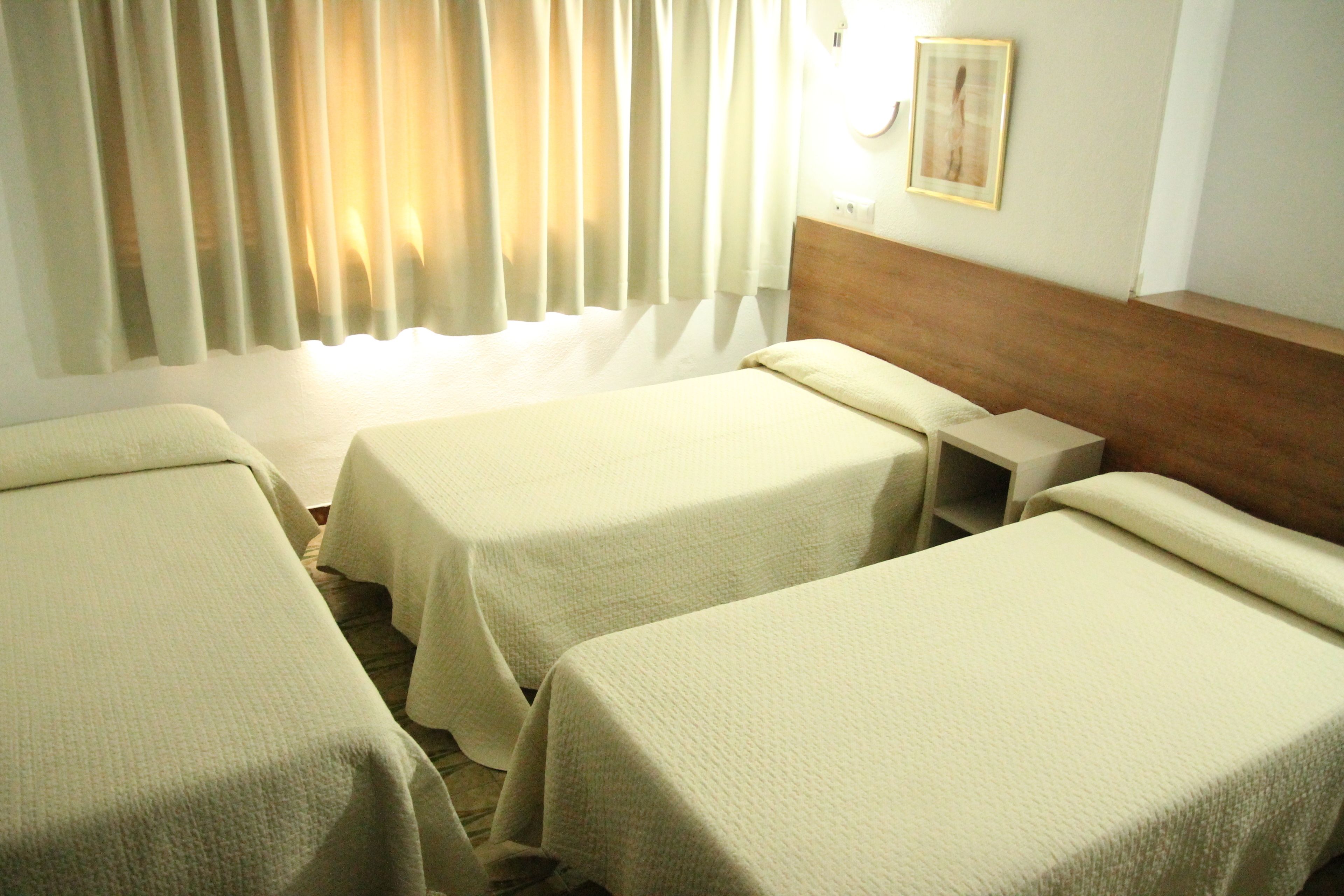 A hotel room with two single beds, a wooden headboard, a bedside table, and a window with curtains.