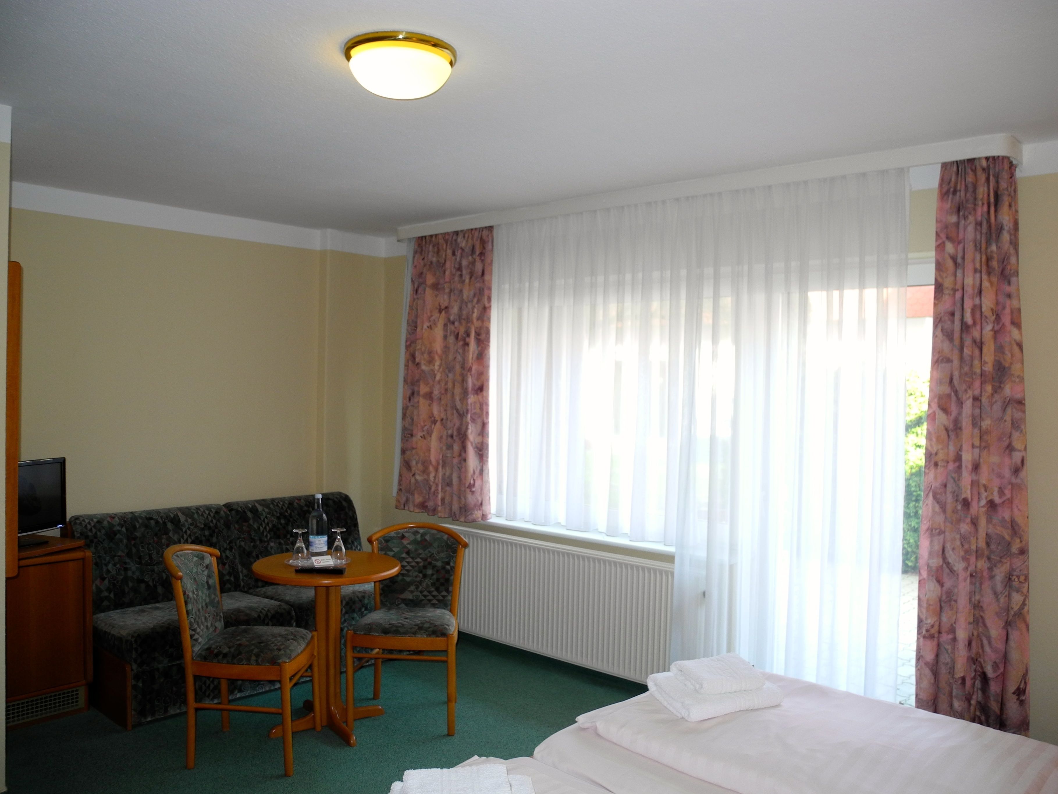 A hotel room with a bed, a sofa, two chairs, a small table, and a television.