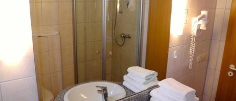 A bathroom with two sinks, a glass shower enclosure, a toilet, and a telephone.