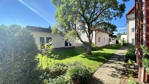 A residential area with a paved pathway, a well-maintained lawn, and a white building with a door and windows. - Hotel Pension Kühne (Boltenhagen)