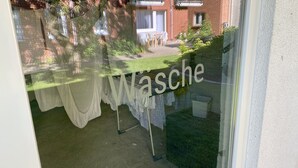 A window with a view of a brick building, a table with clothes, and a sign reading "Wasche". - Hotel Pension Kühne (Boltenhagen)