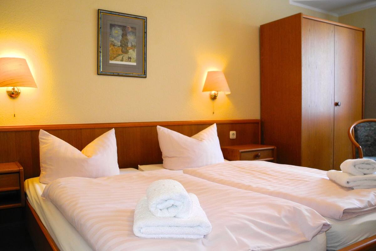 Habitación de hotel con dos camas, un armario de madera y dos lámparas fijadas a la pared.