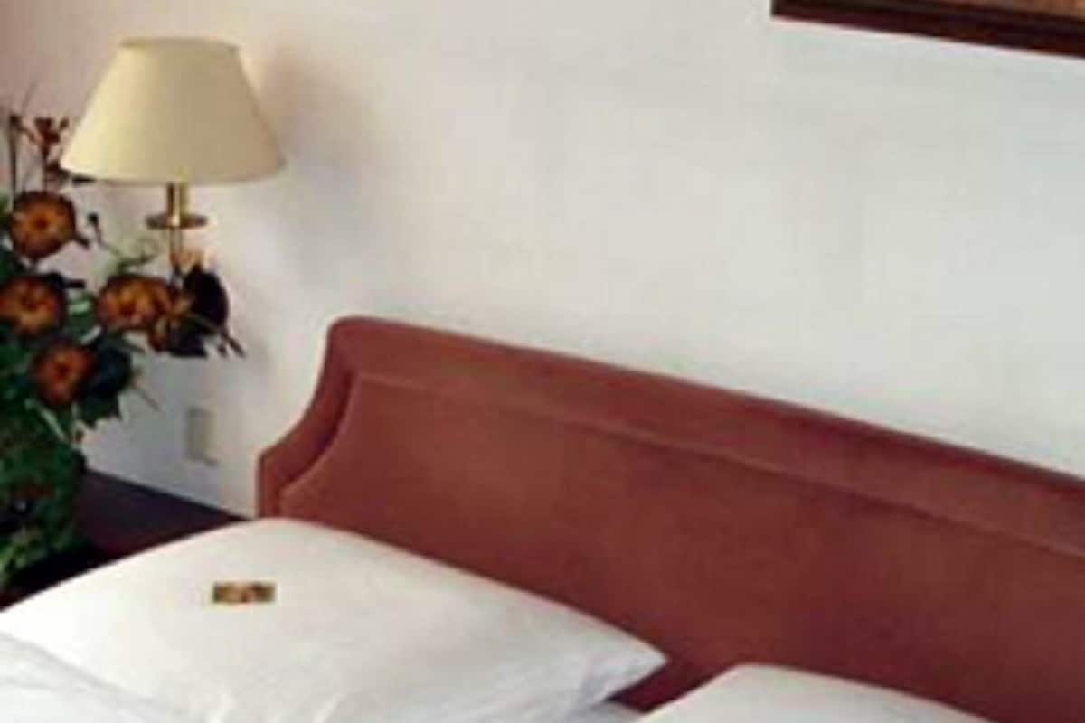 Ein Hotelzimmer mit zwei Betten, einem Holzkopfteil, einer Lampe und einer Vase mit Blumen.