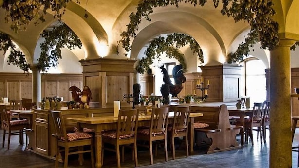 Ein Essbereich mit Holztischen und -stühlen, einer zentralen Statue und Bögen mit hängenden Pflanzen.