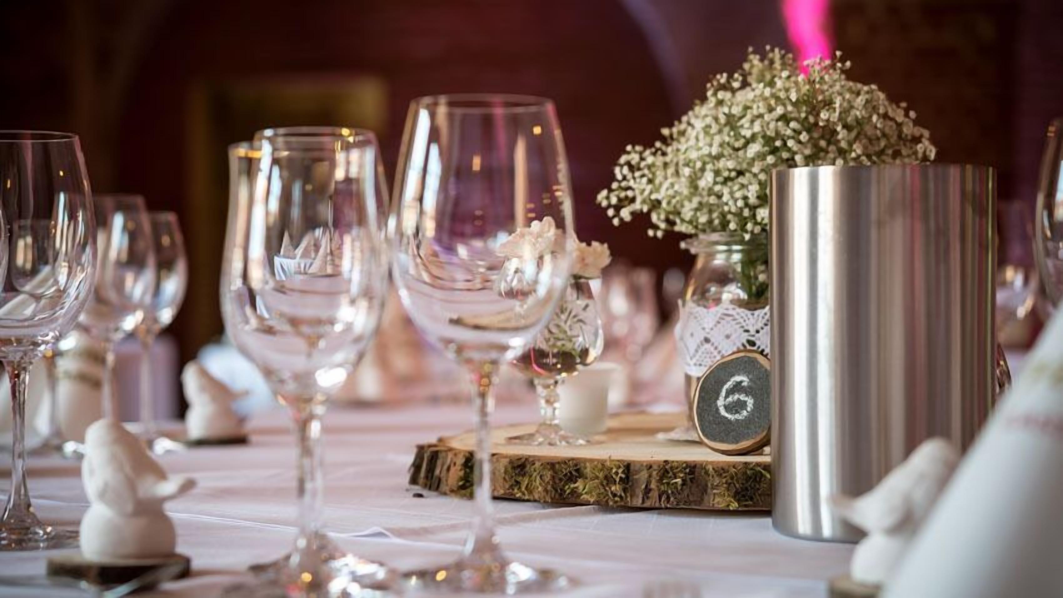 Et bord dækket med vinglas, en dekorativ vase med blomster og en nummereret underkop.