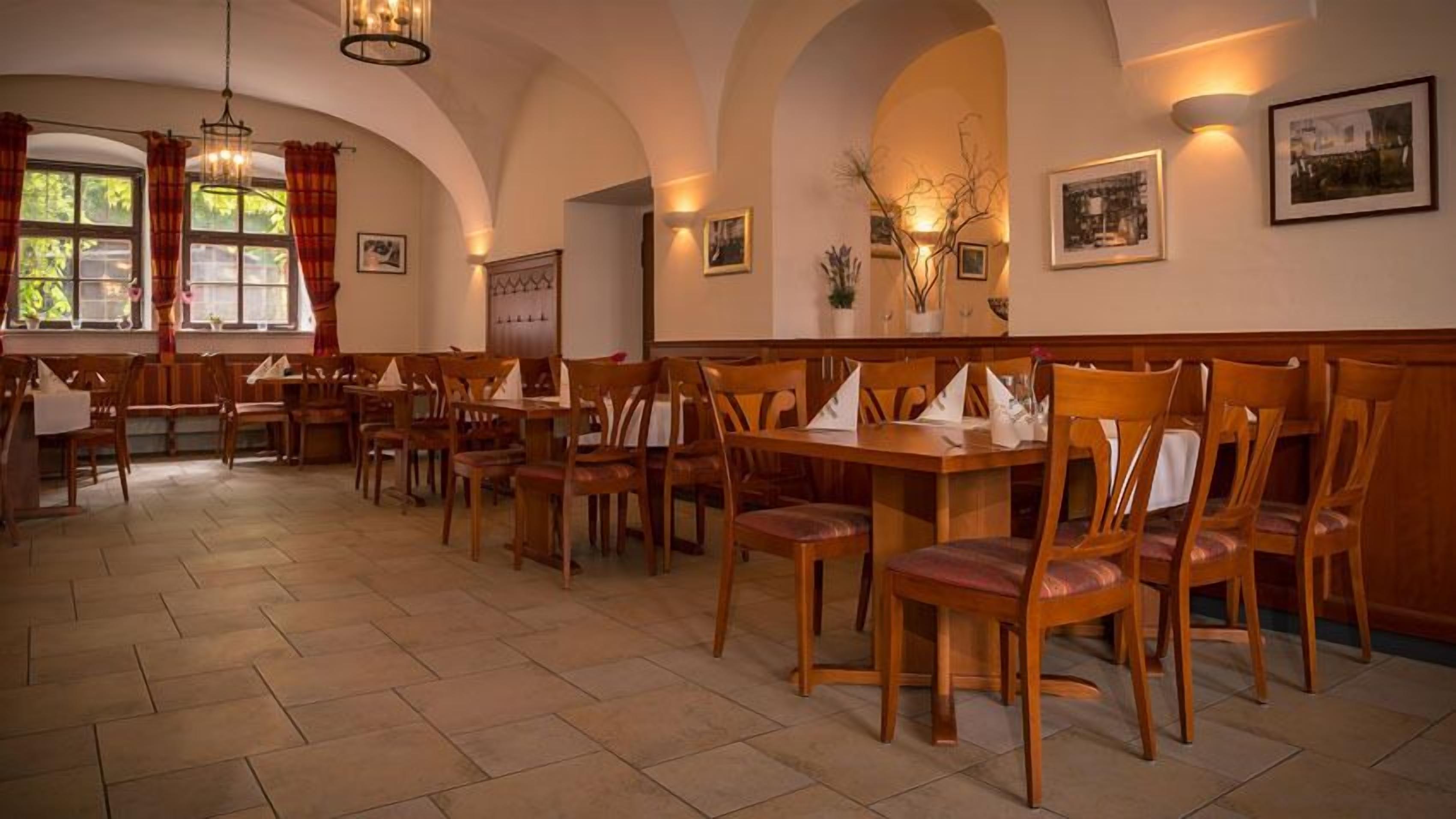 A restaurant with wooden tables and chairs, arched ceilings, and wall-mounted lighting.