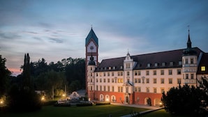 Ein großes, historisches Gebäude mit einem markanten Glockenturm und einer zentralen Kuppel, umgeben von gepflegten Gärten und Wegen.