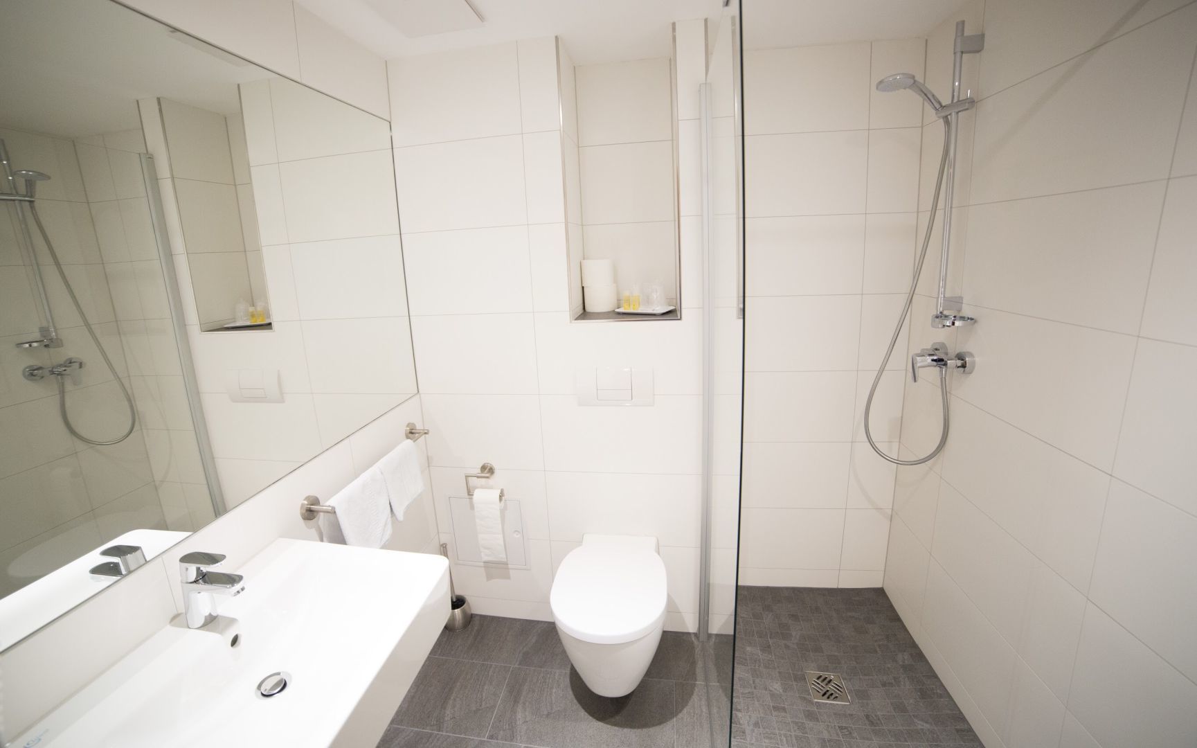 Un baño moderno con lavamanos, inodoro y zona de ducha blancos.