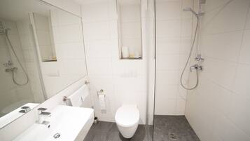Un baño moderno con lavamanos, inodoro y zona de ducha blancos.