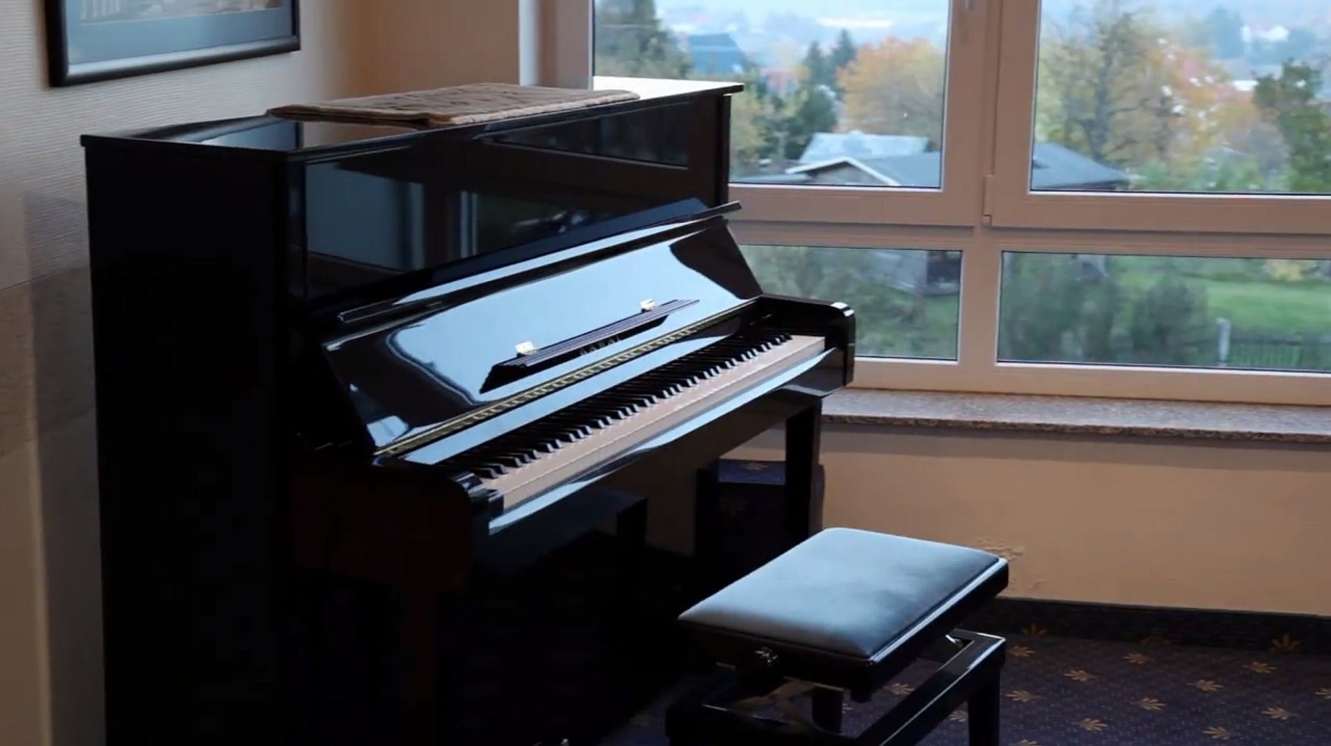 A black upright piano with a bench in a room with a large window.