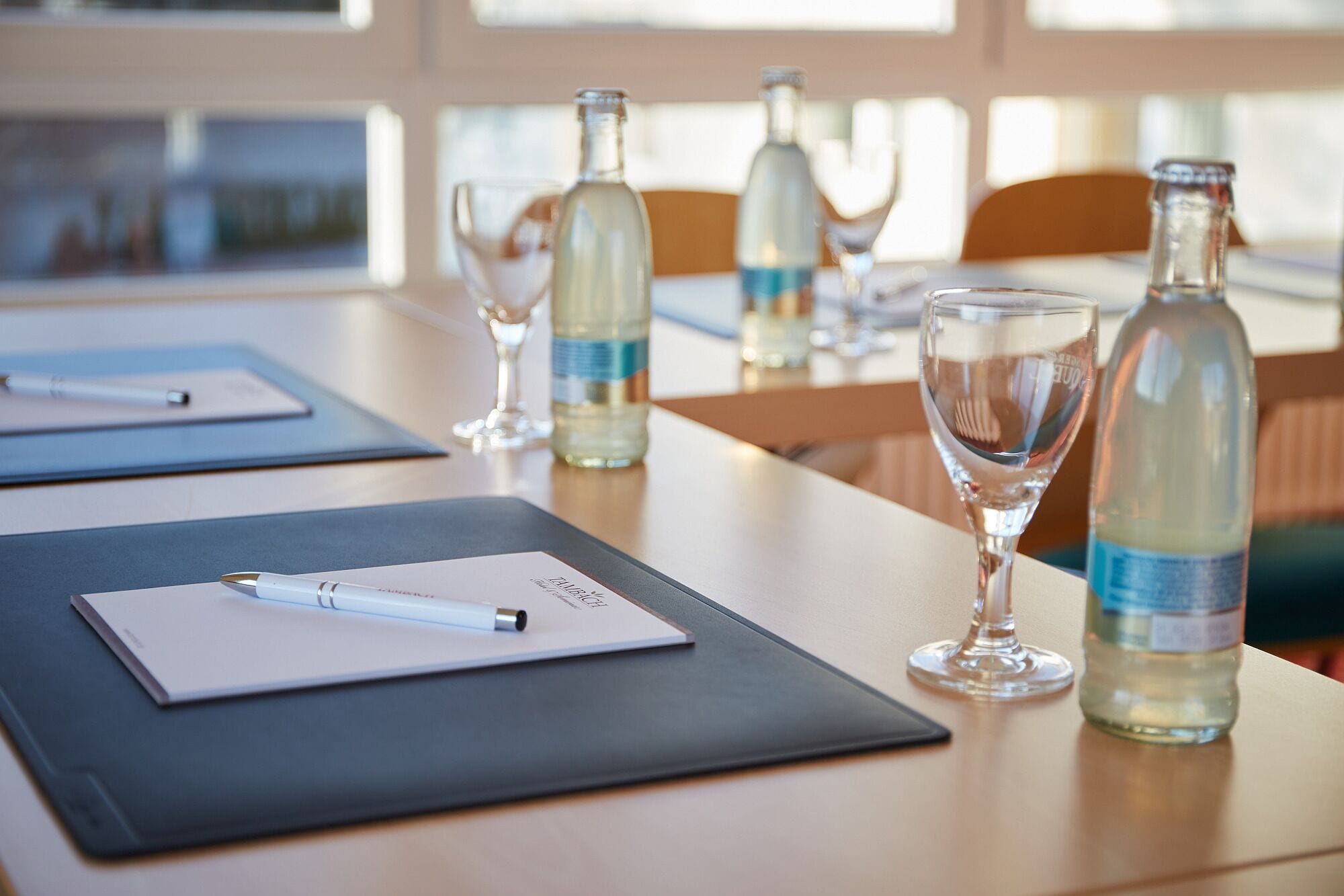 A conference table with a notebook, pen, wine glass, and bottles.
