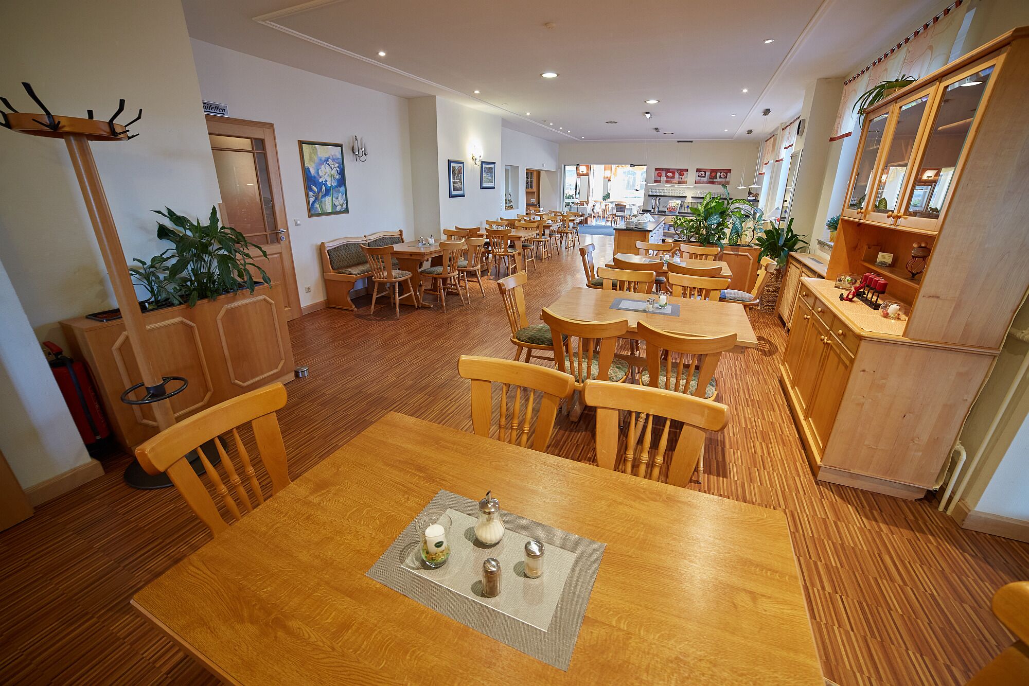 Un grand espace dédié à la salle à manger, avec plusieurs tables et chaises en bois, un buffet en bois doté d’un miroir et des plantes en pot.