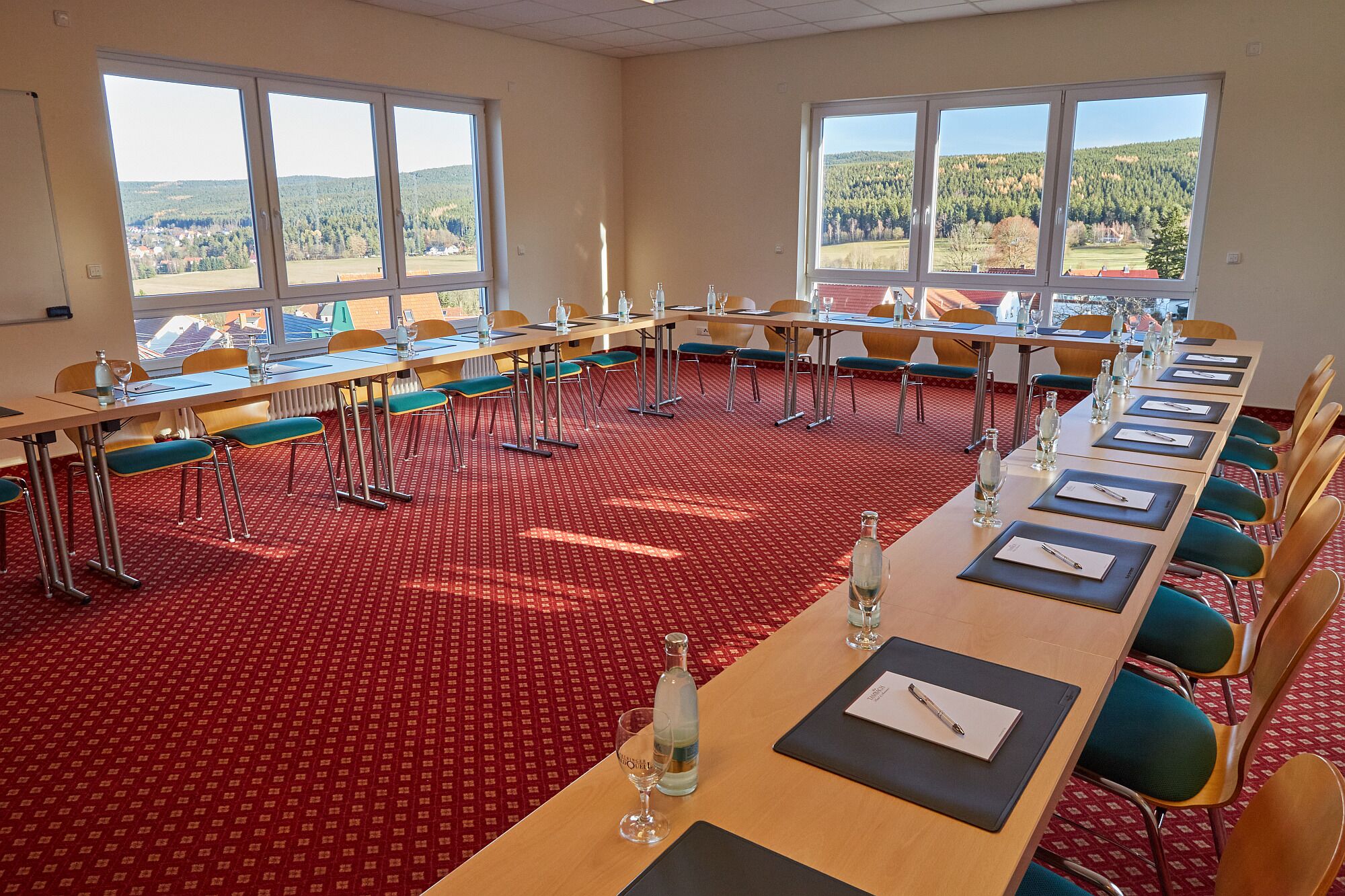 A conference room with long tables, chairs, and large windows offering a view of a forested landscape.