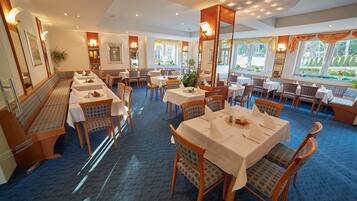 A restaurant with multiple tables and chairs, a blue carpeted floor, and large windows with views of greenery.